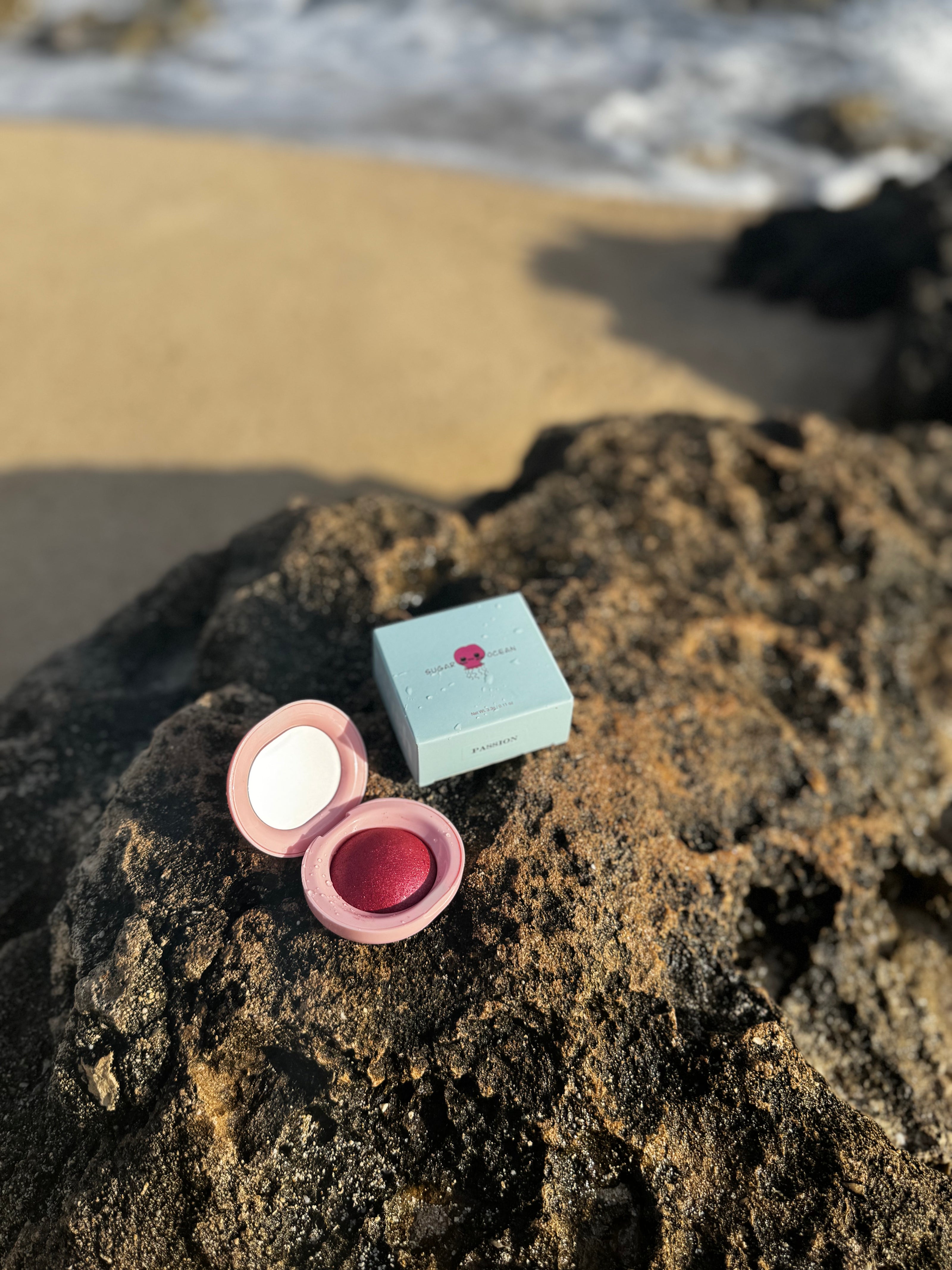 Makeup compact and case on a rocky beach with ocean waves in the background