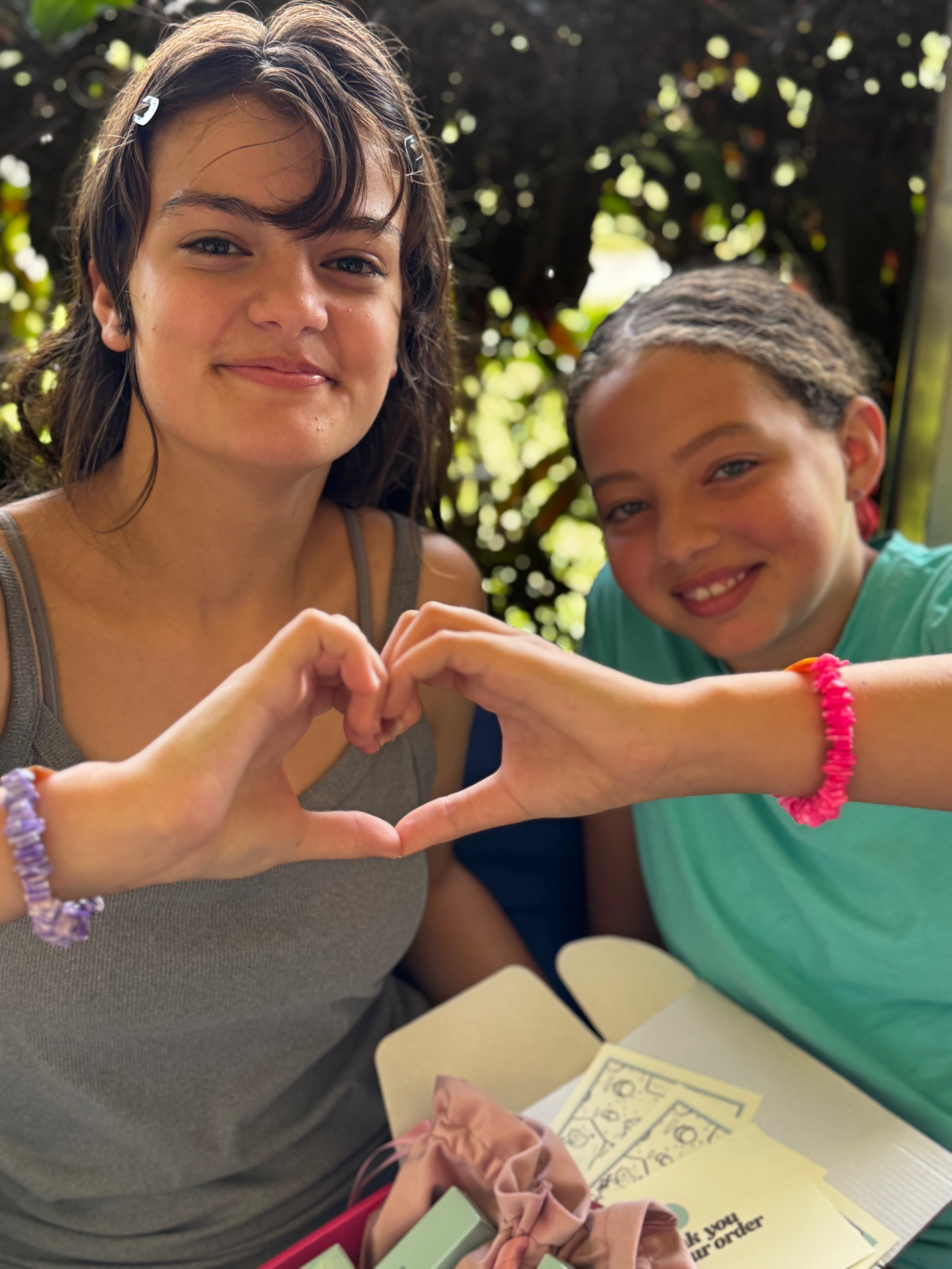 Translation missing: en.Two young girls making a heart shape with their hands outdoors